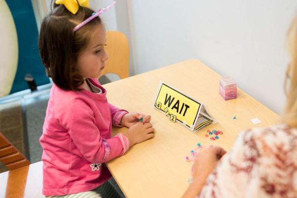 A young girl at a table with a card that reads WAIT, placing small beads