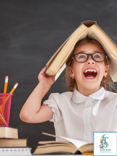 A laughing girl in glasses holding an open book on top of her head